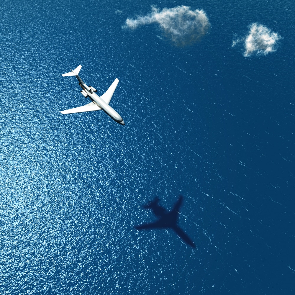Commercial passenger jet flying over open ocean with shadow cast on deep blue water below