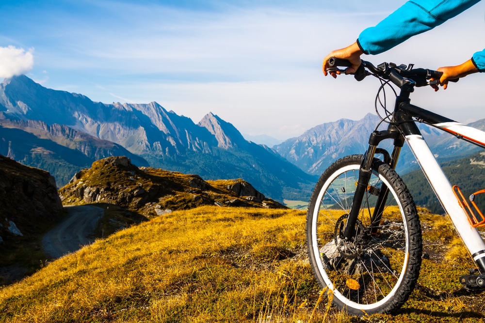Mountain biker holding handlebars on alpine meadow with dramatic Rocky Mountain peaks in background