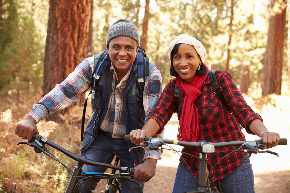 Senior couple mountain biking on a forest trail, embracing an active retirement lifestyle with confidence