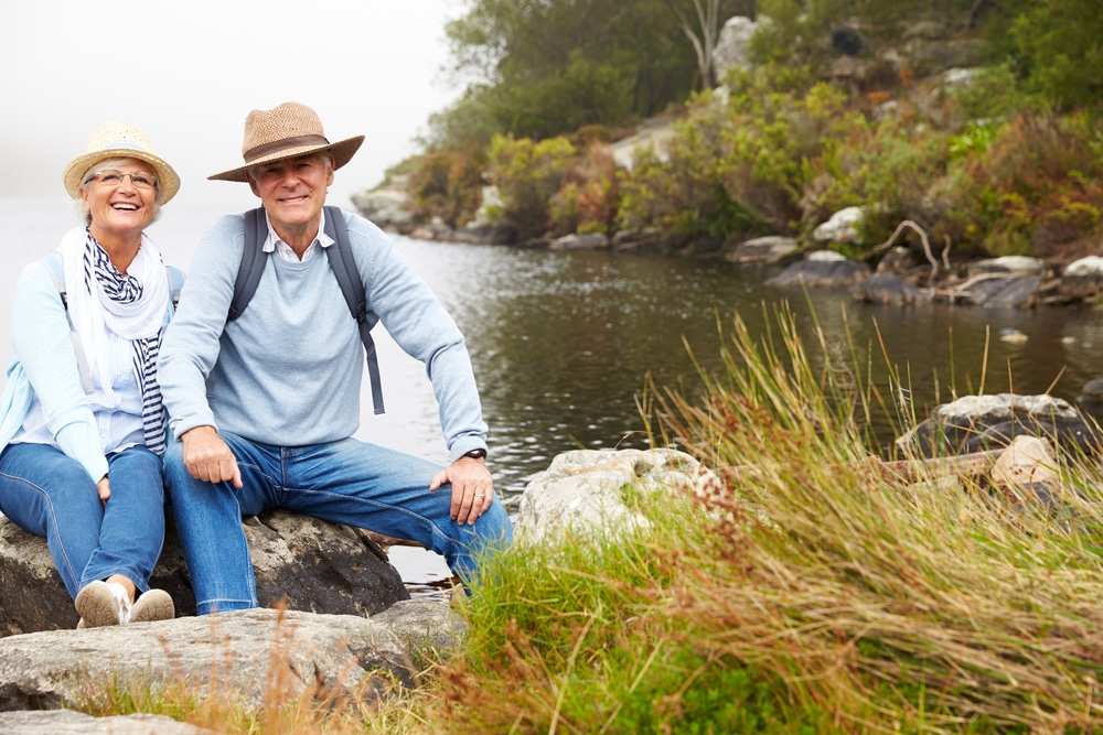 Retired couple sitting on rocks by a calm Alberta lake, smiling and enjoying outdoor recreation together