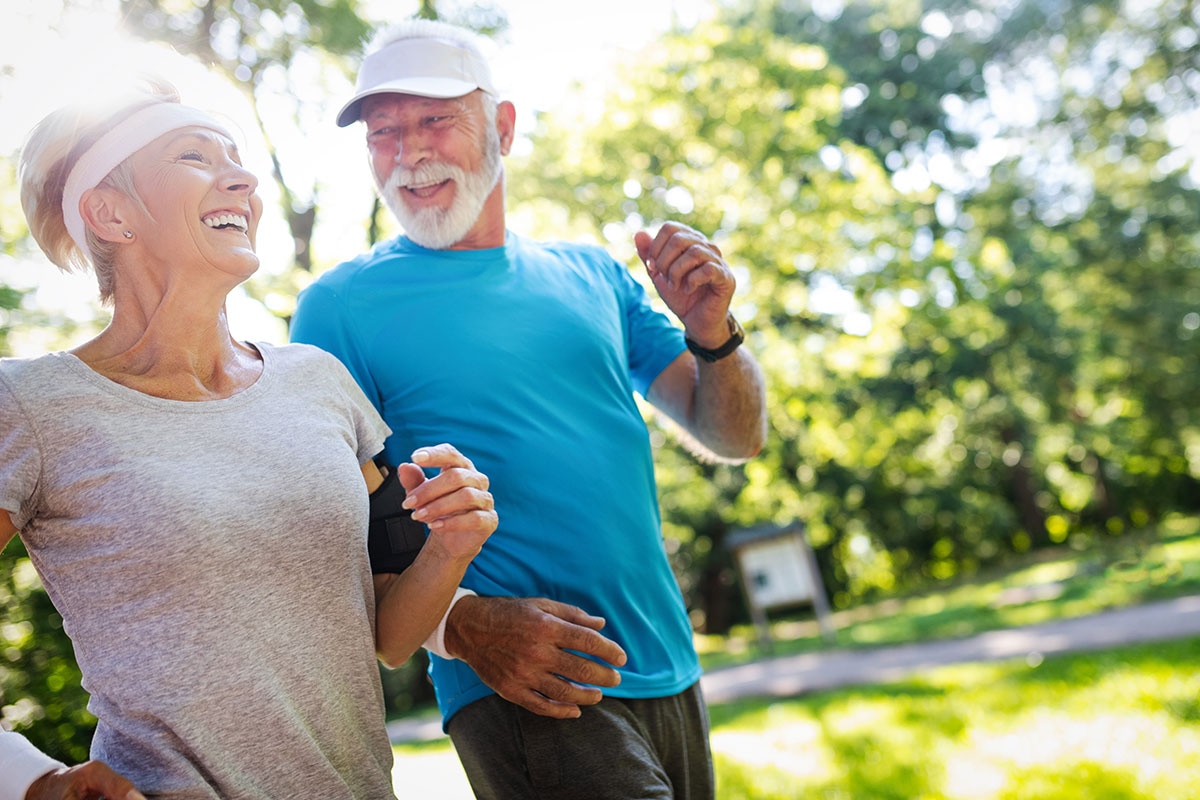Retired couple jogging together in a sunny park, staying active and healthy in their 60s with ASEBP MyRetiree Plan coverage