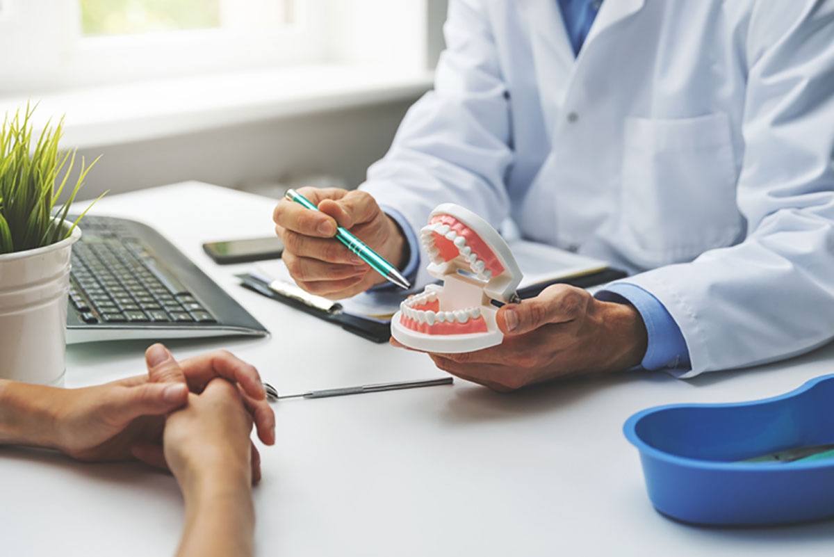 Dentist pointing to jaw model to help patient understand dental fee guide and coverage during appointment