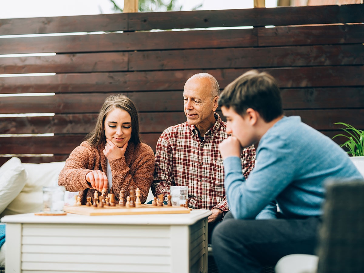 Retired grandfather playing chess with grandchildren on a sunny patio, enjoying active retirement in Alberta