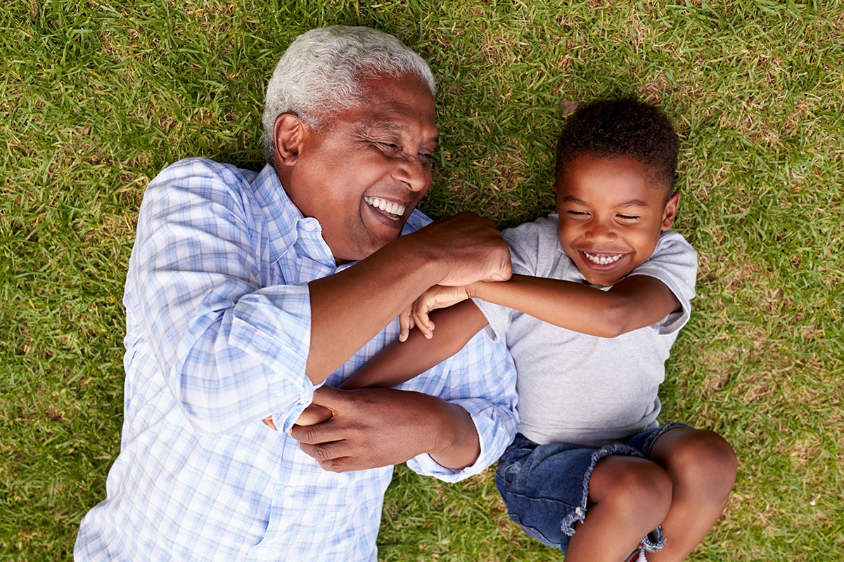 Grandfather and grandson laughing together on green grass, enjoying active retirement with ASEBP MyRetiree Plan coverage