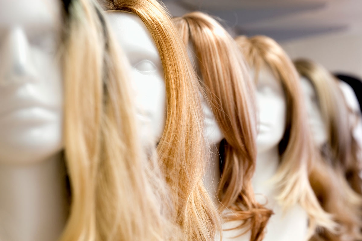 Row of mannequin heads displaying long blonde and auburn hairpieces covered under ASEBP MyRetiree Plan benefits