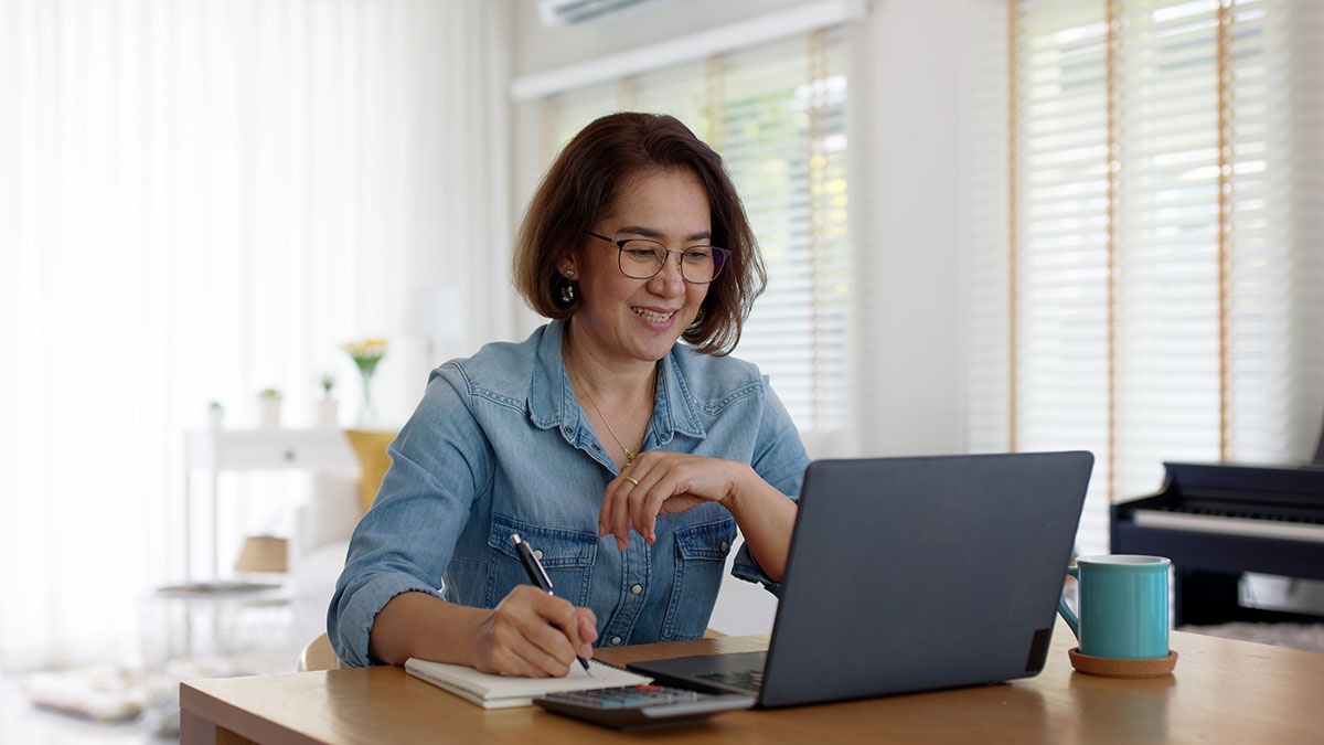 Retired Alberta educator smiling while researching ASEBP MyRetiree Plan health benefits on laptop at home desk