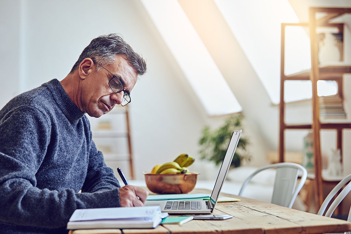 Retired Alberta educator carefully completing MyRetiree Plan premium payment paperwork at home desk with laptop nearby