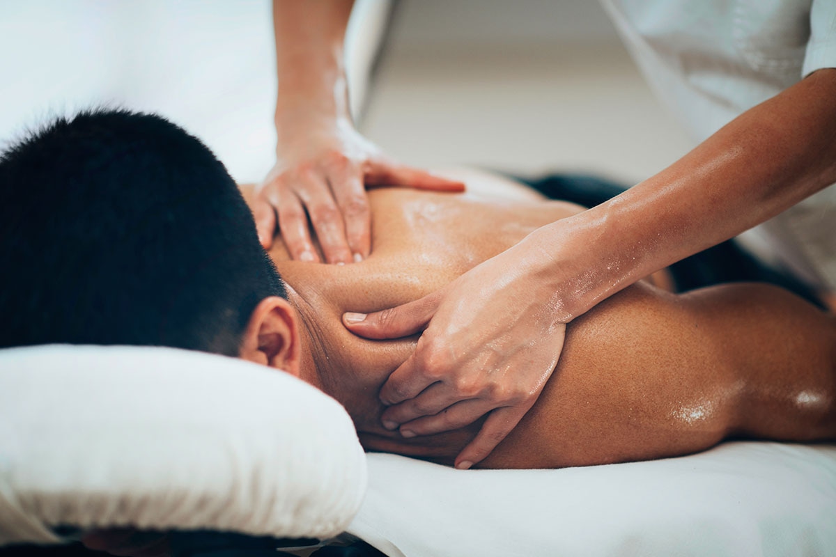 Professional massage therapist performing deep tissue massage on client's upper back and shoulders in a clinical spa setting