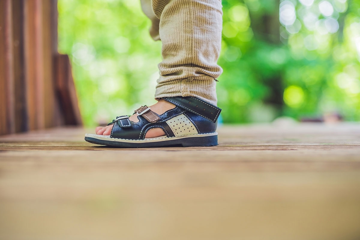 Child's foot in navy leather orthopedic sandal on wooden deck, representing orthopedic shoe coverage under ASEBP MyRetiree Plan