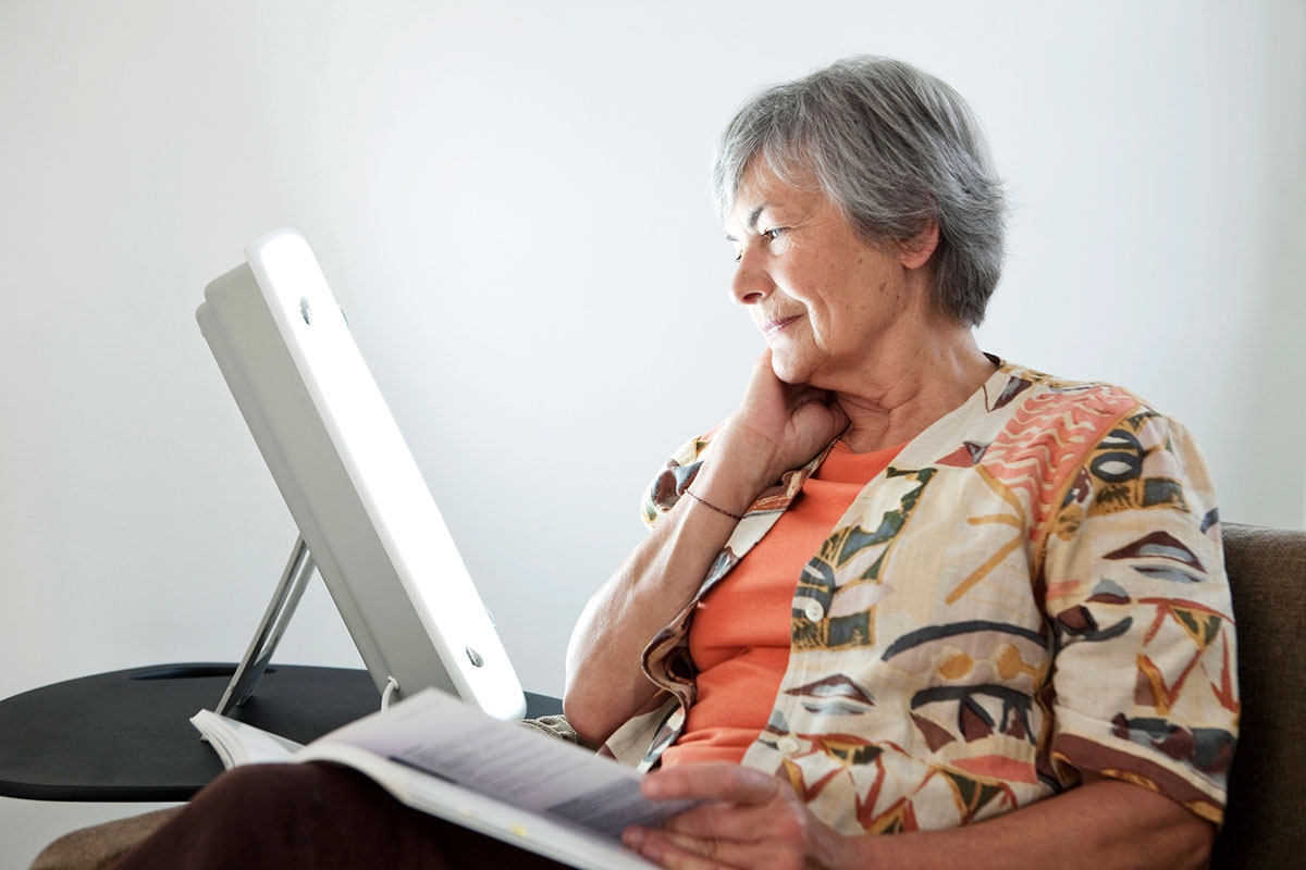Senior woman sitting with a light therapy lamp, taking advantage of her retiree health benefits coverage