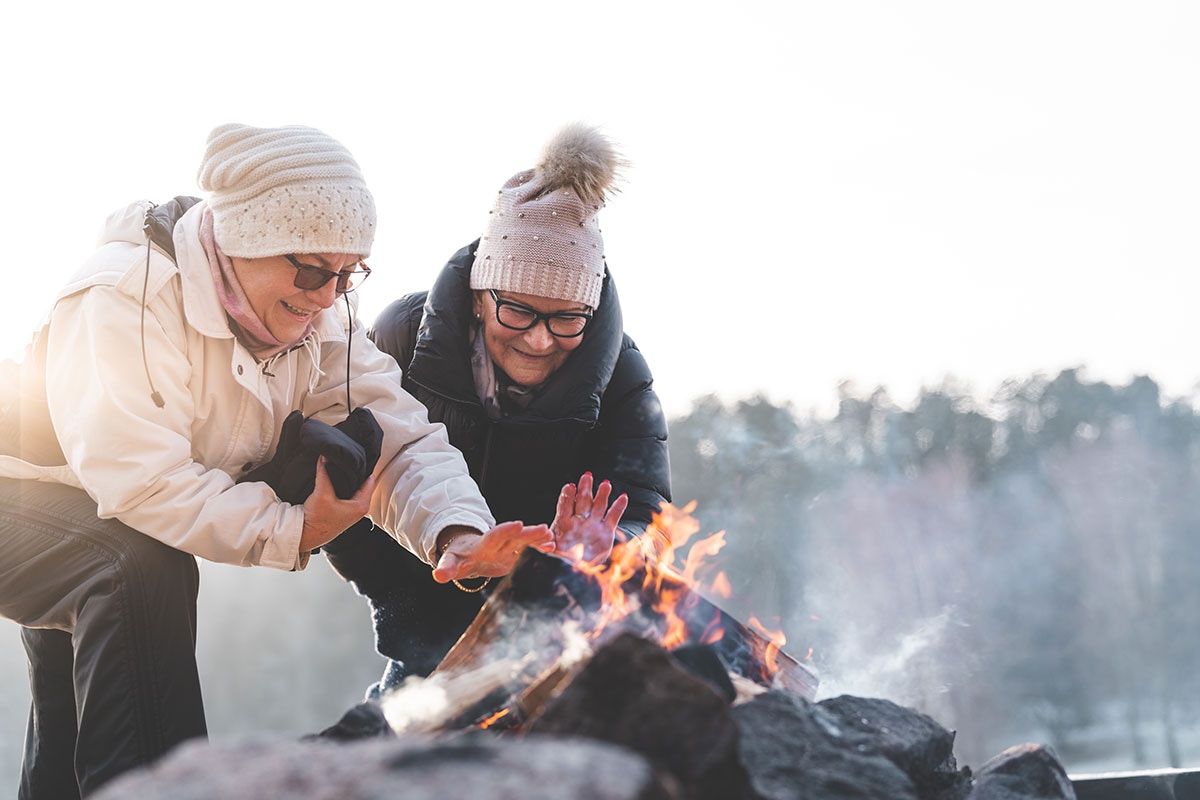 Senior women leaning over a winter campfire together, representing the active retirement lifestyle MyRetiree Plan helps protect