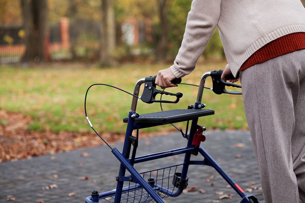 Senior using a blue rollator walker with hand brakes and storage basket during an autumn outdoor walk