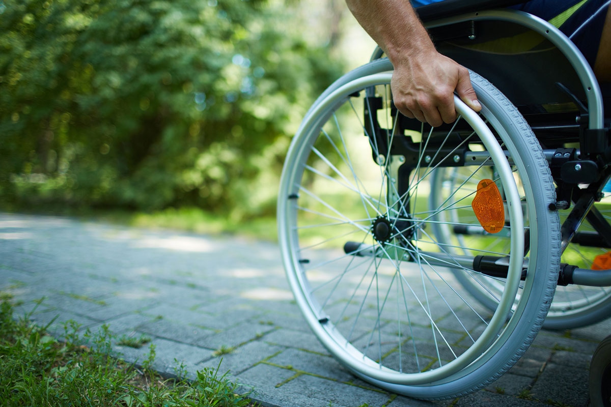 Person self-propelling a manual wheelchair along an outdoor stone pathway, gripping the hand rim