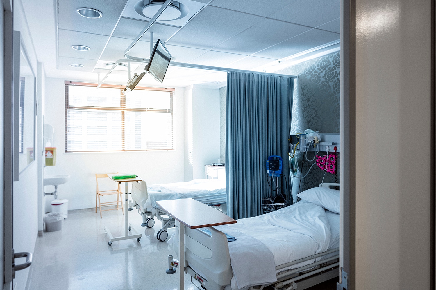 Bright, modern semi-private hospital room with two beds, medical equipment, and natural light streaming through window