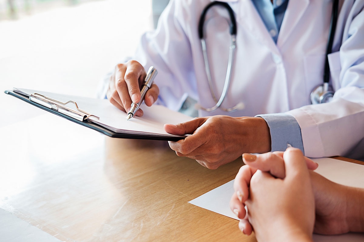 Doctor writing notes on clipboard during patient consultation for specialty drug authorization in Alberta