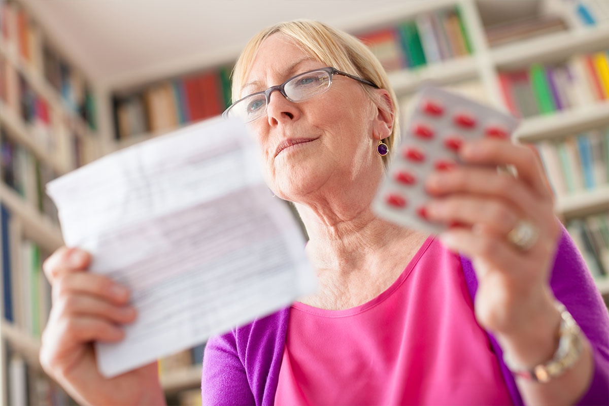 Retired woman comparing prescription medication leaflet with blister pack of pills at home