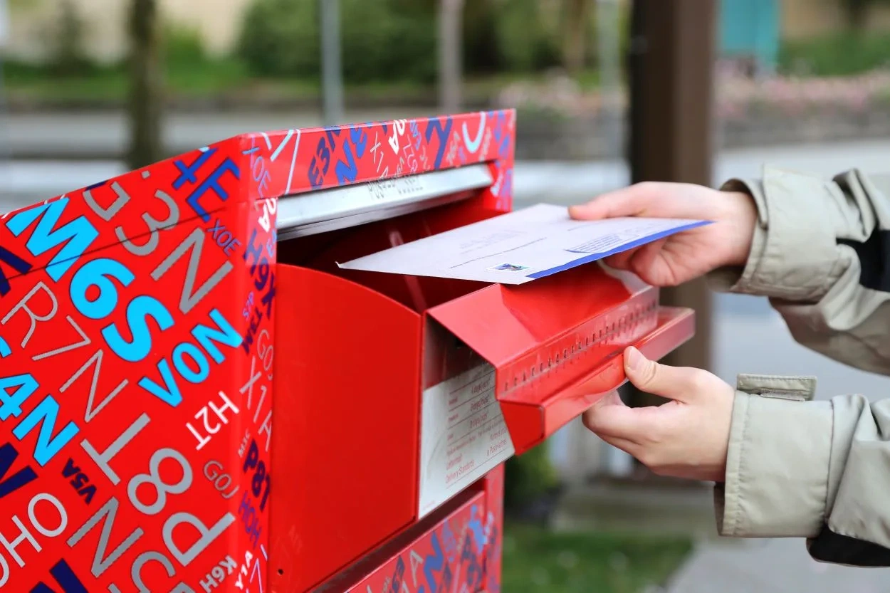 Person mailing an envelope in a decorated red Canada Post mailbox in an outdoor urban setting