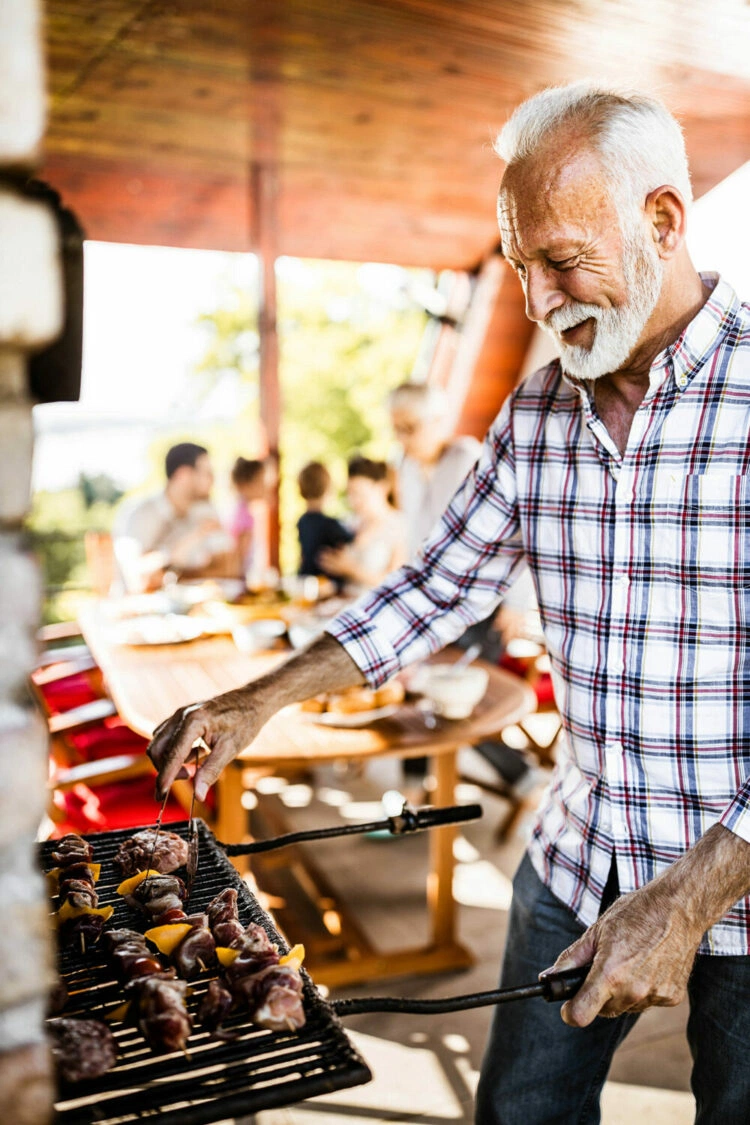 Retired senior man grilling skewers at a family outdoor barbecue, smiling and enjoying retirement life in Alberta